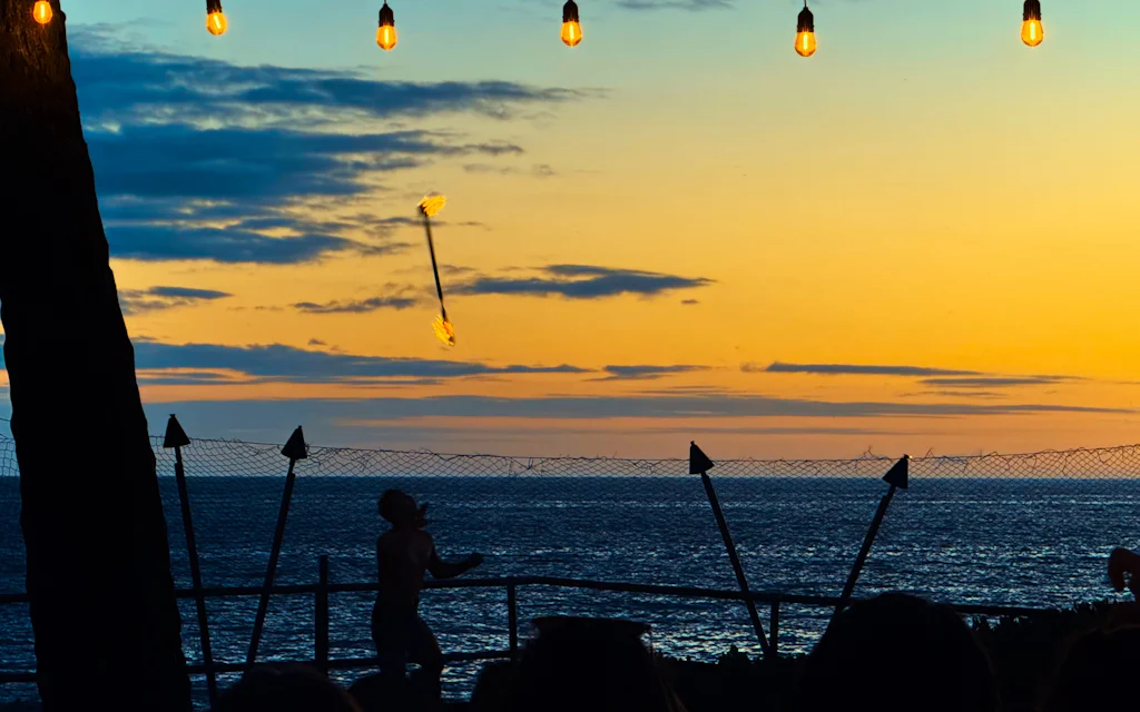 Tiki torches lit at sunset over the ocean at a Maui luau