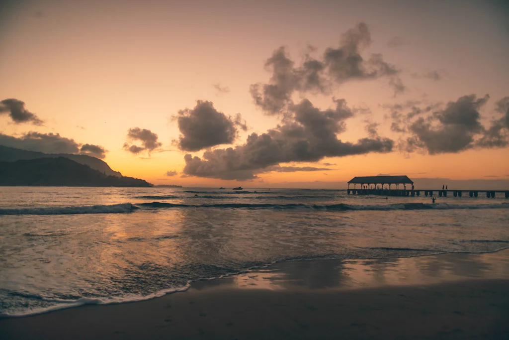 Sunset over Hanalei Bay and the historic Hanalei Pier on the north shore of Kauai, the green mountains rising behind the crescent beach
