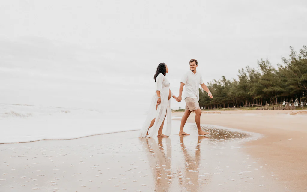 A couple in light beach outfits walking on the sand in Hawaii