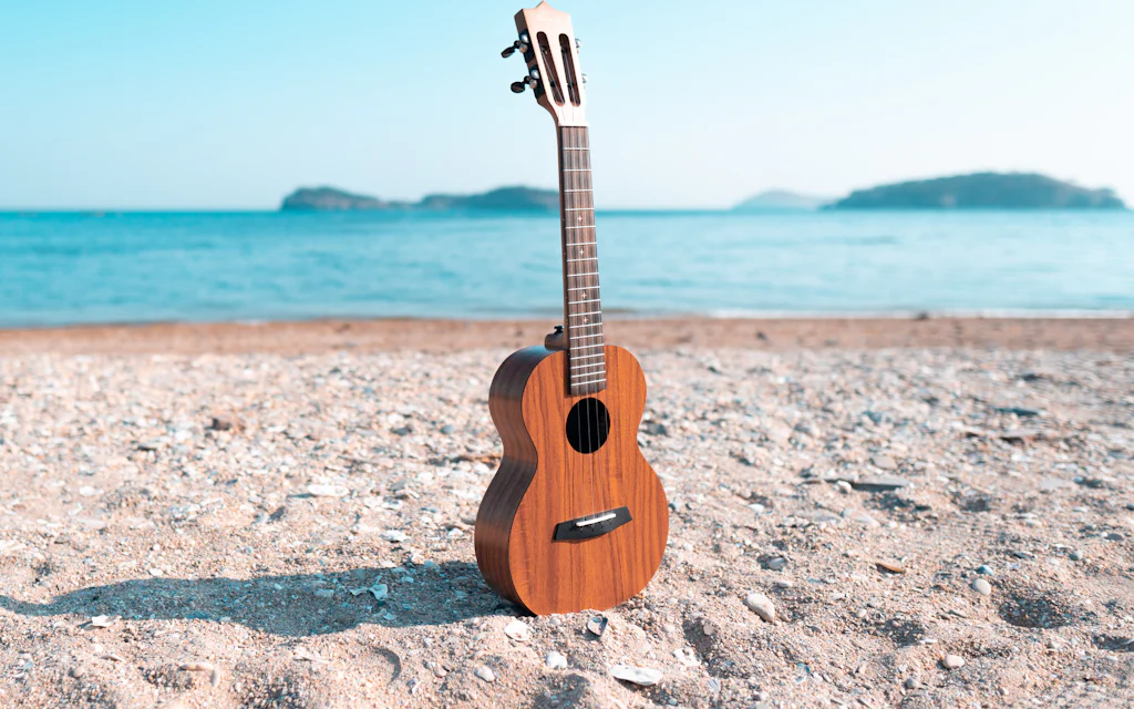 A wooden ukulele resting on a sandy beach in Hawaii