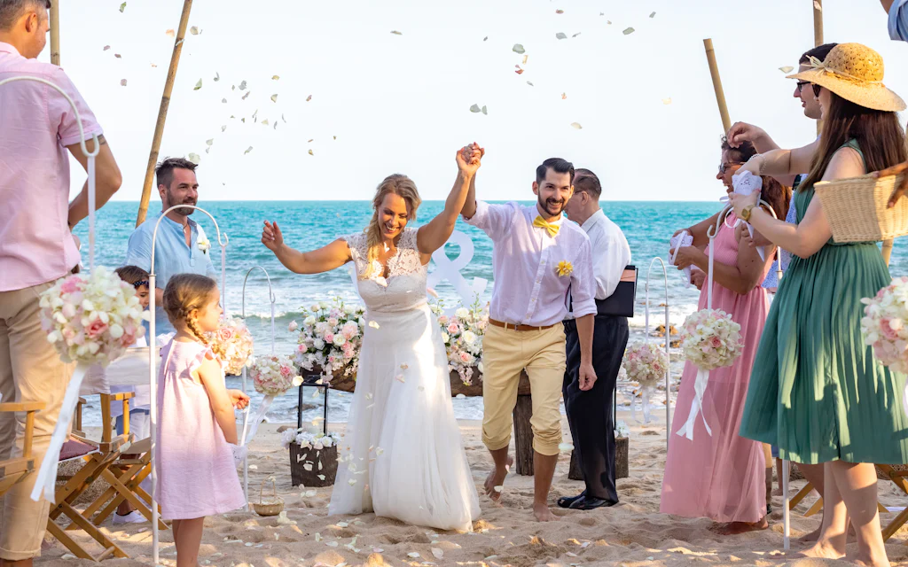 A couple celebrates getting married in Hawaii as guests toss petals on a sunny beach