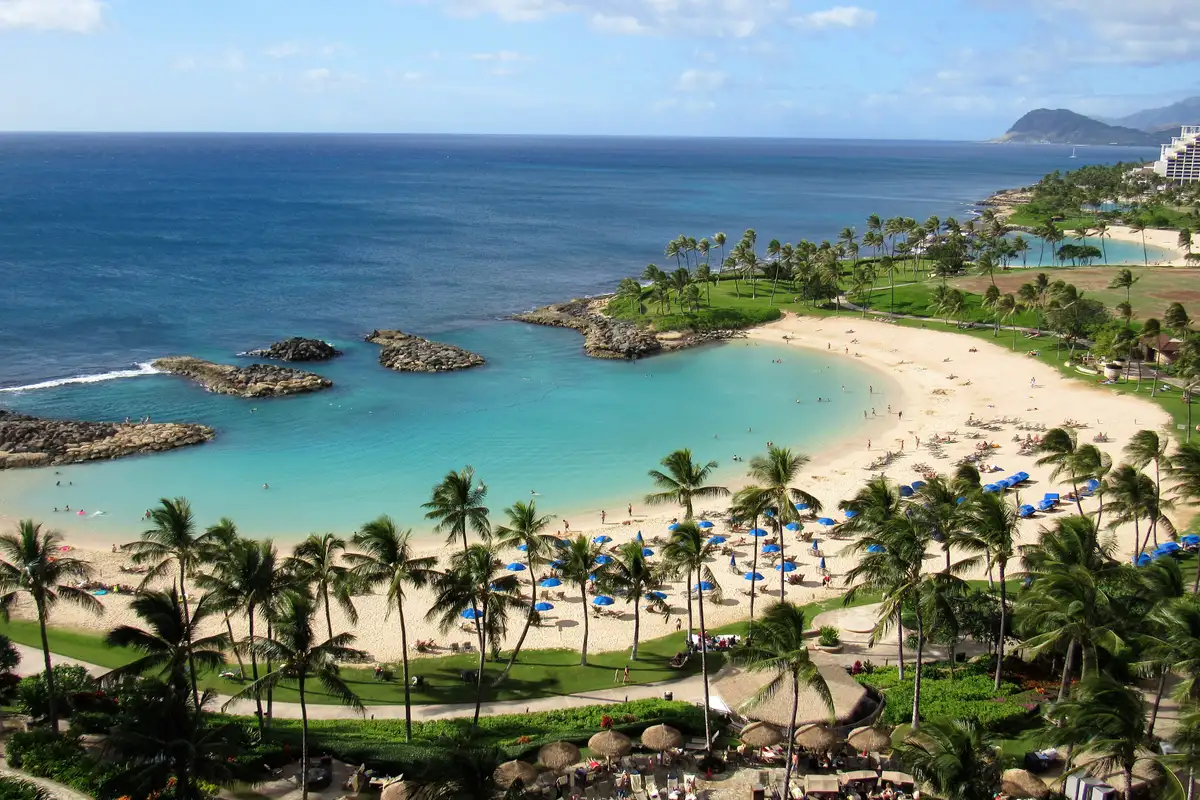 A Ko Olina lagoon on Oahu's west side, calm clear water behind a rock breakwater with palms and white sand