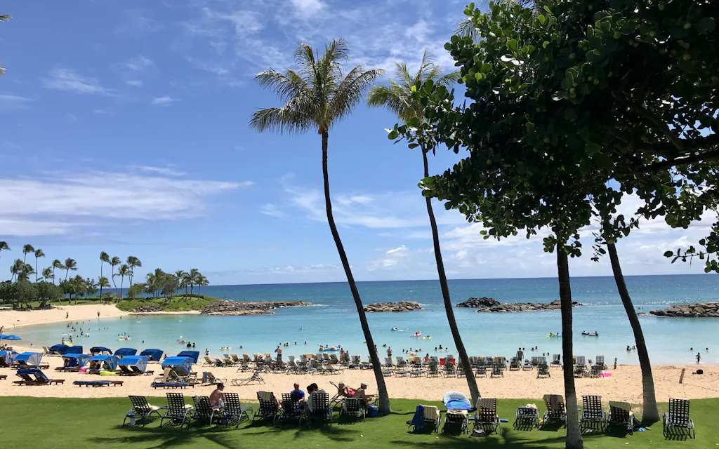 A Ko Olina lagoon on Oahu's west side, a calm half-moon beach with palms, chairs, and a rock breakwater
