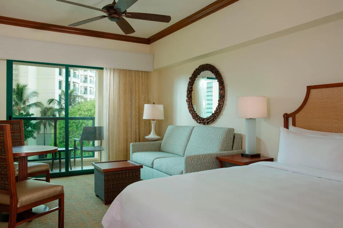 A Marriott Ko Olina Beach Club room with a sofa bed, dining table and a lanai over the palms