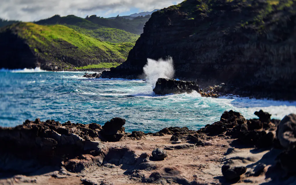 Surf exploding off the lava-rock point below green cliffs on Maui's north coast near the Nakalele Blowhole