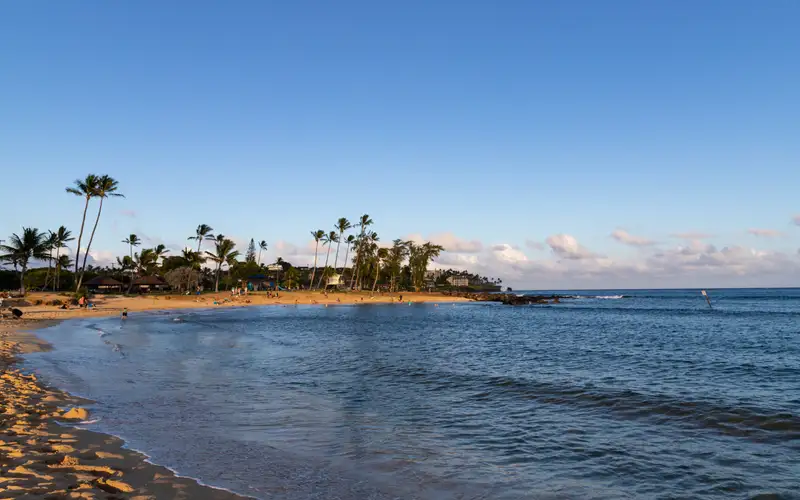 Poipu Beach on Kauai's sunny south shore, a calm gold-sand bay with palms and resorts behind