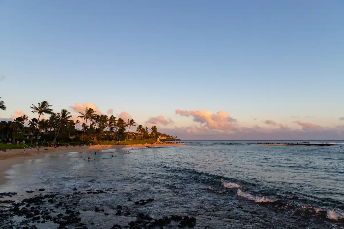 Golden hour light over Poipu Beach with palms and the south shore resorts behind