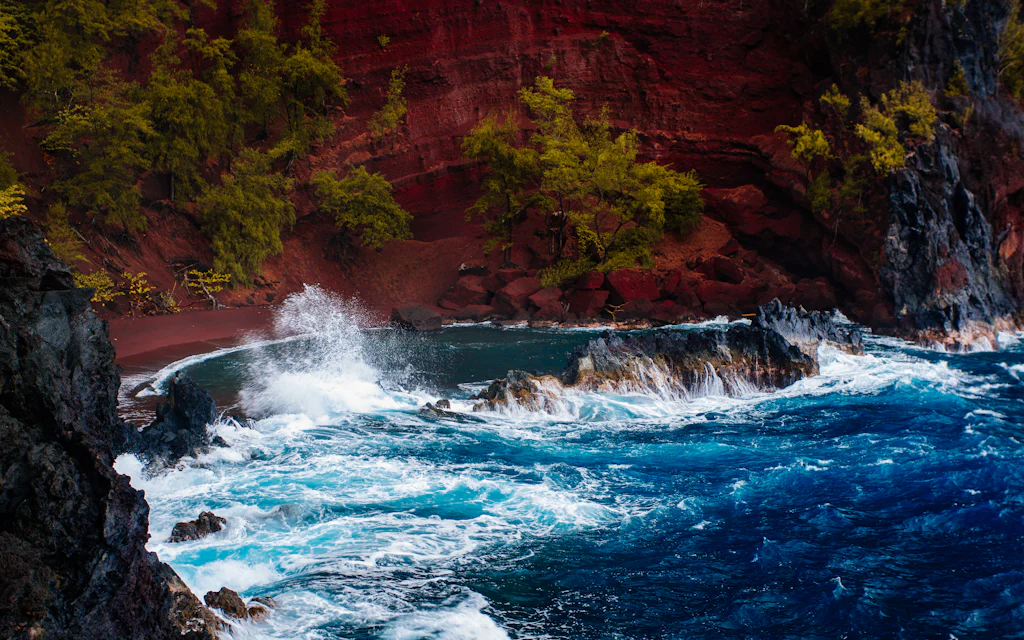 Red Sand Beach Maui, the Kaihalulu cove with rust red cliffs, black lava sea wall, and deep blue surf near Hana