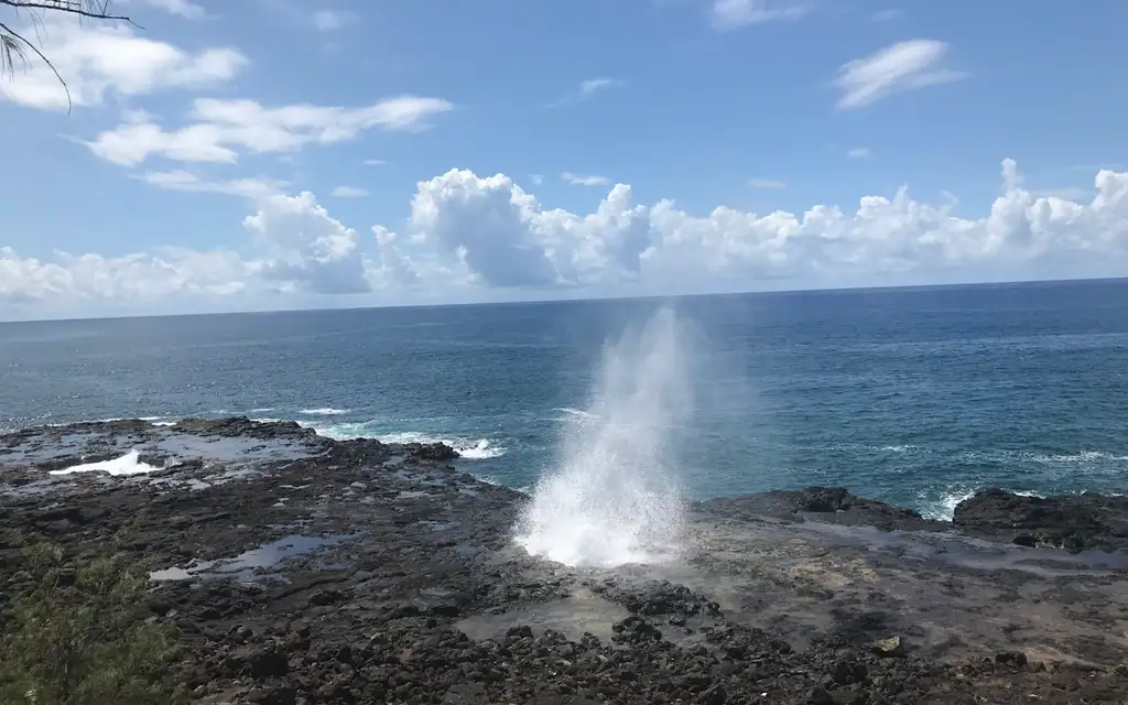 Spouting Horn Kauai blowhole shooting a fan of seawater up from the lava shelf on the south shore at Poipu under a blue sky