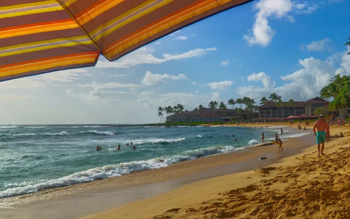 Poipu Beach on Kauai's south shore, a golden-sand bay five minutes from Spouting Horn, with swimmers and the south shore resorts behind