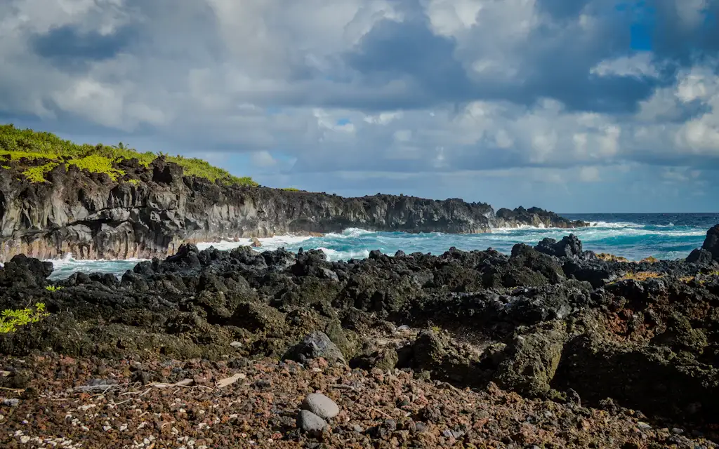 The rugged black lava-rock coastline and crashing surf of East Maui near Hana, where Waioka Pond (the Venus Pools Maui) meets the sea