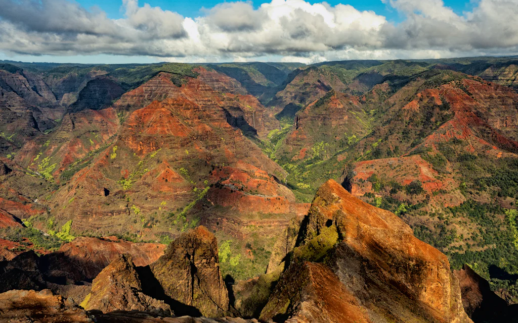 An aerial view of the red and green cliffs of Waimea Canyon on Kauai